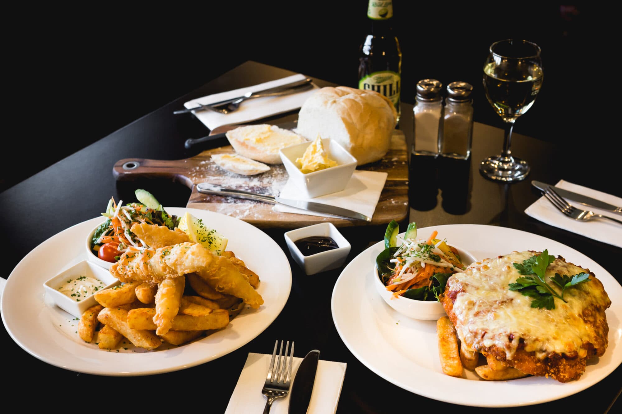 A chicken parmigiana and a seafood basket with bread and drinks, set on a bistro table